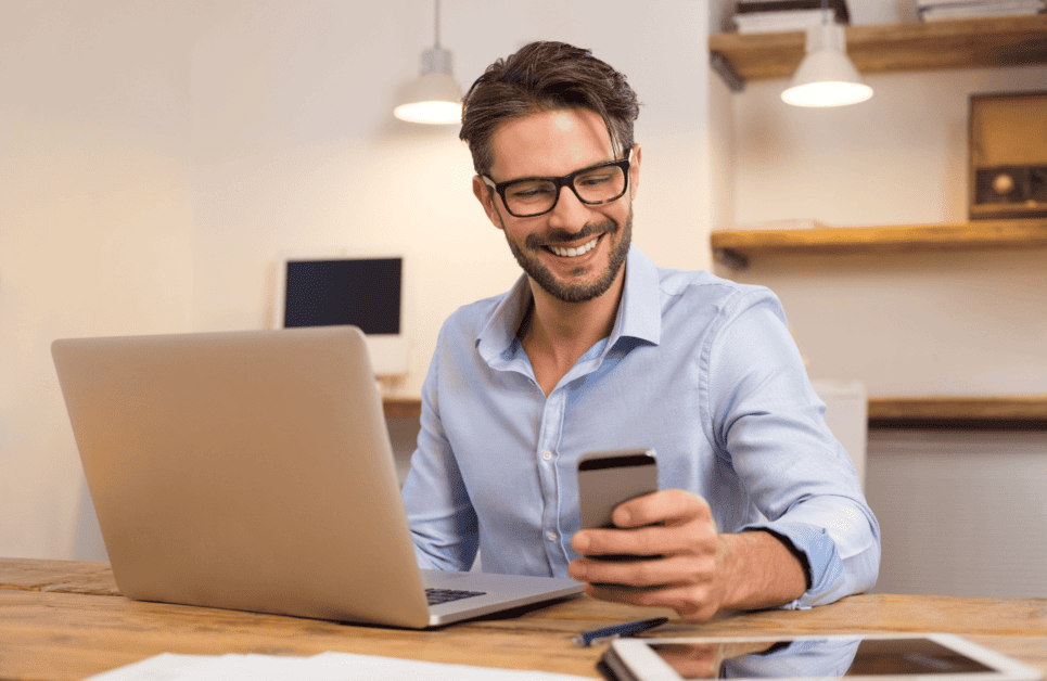 uomo sorridente al portatile guarda smartphone